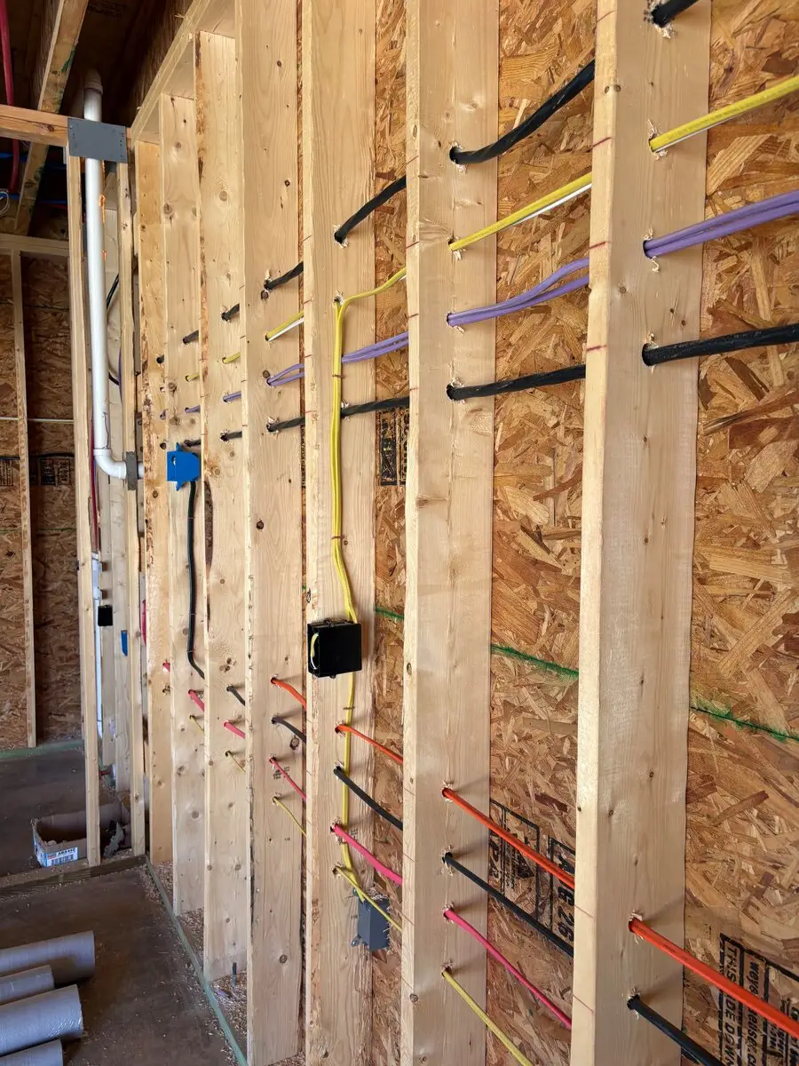 Colored wires run through holes drilled in a row of wall studs