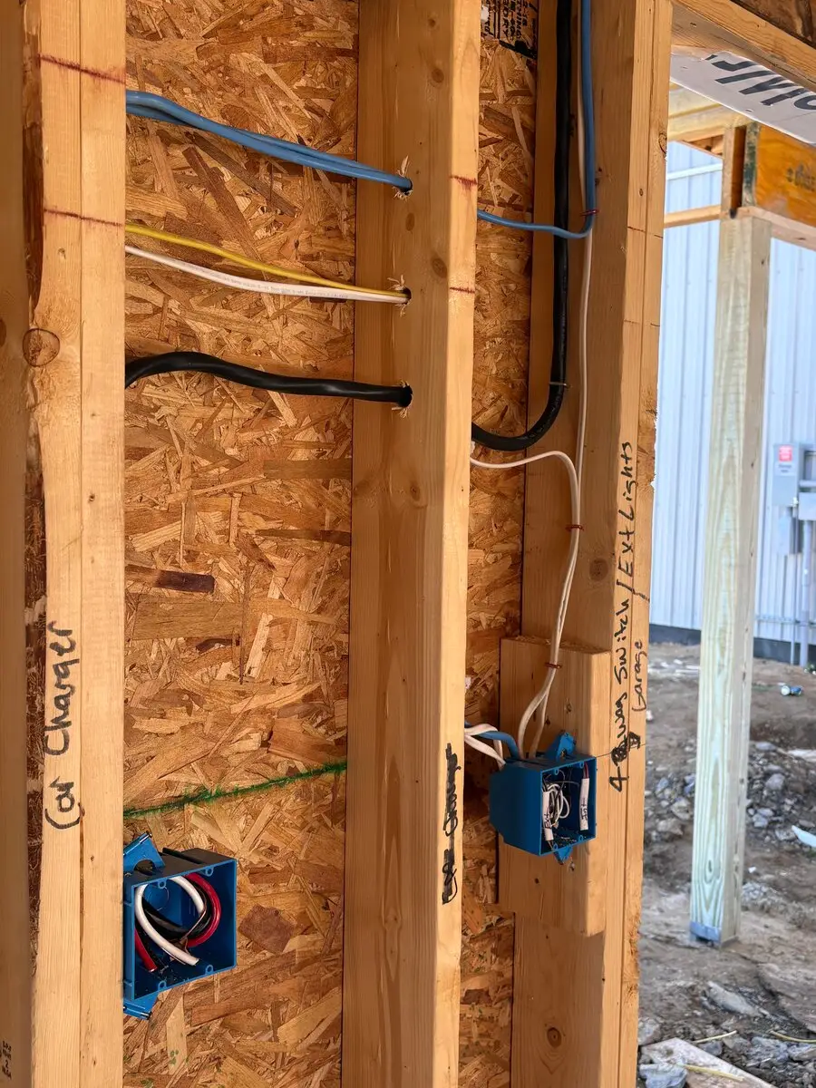 Blue electrical boxes on wall studs, with handwritten labels on the studs