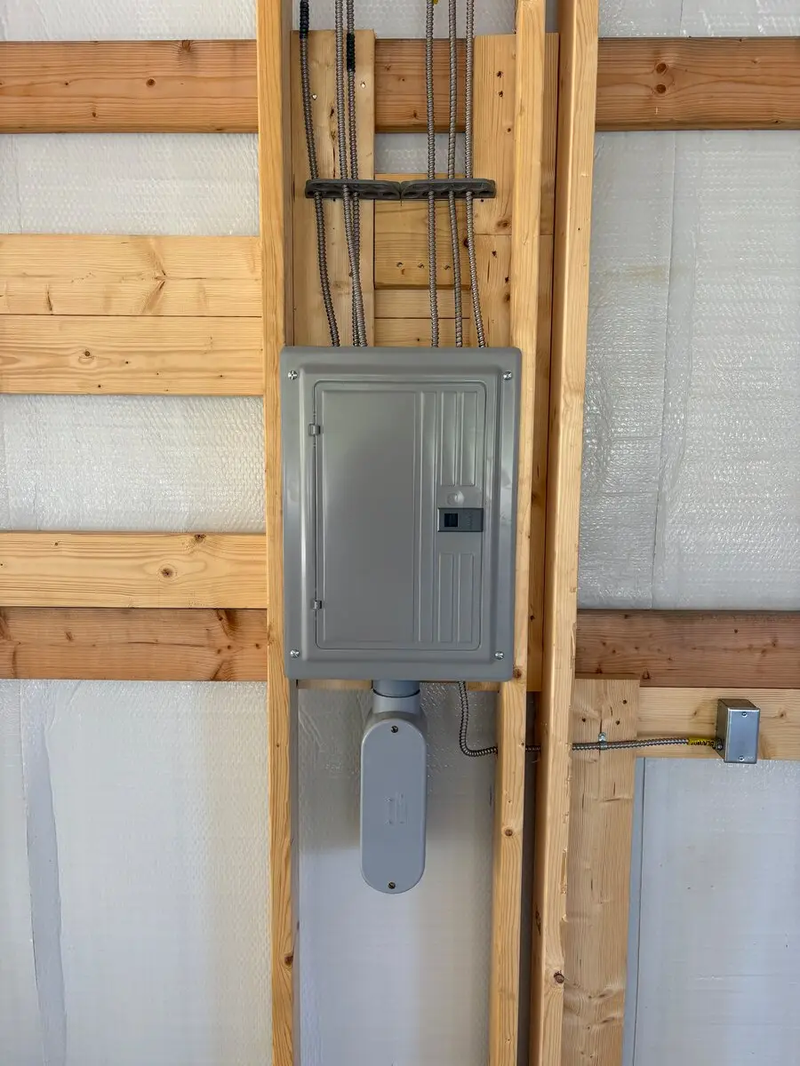 Gray electrical panel mounted between wall studs with cables running into the top