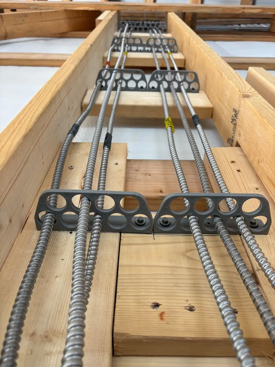 Metal-sheathed cables running along wooden framing, held in place by brackets