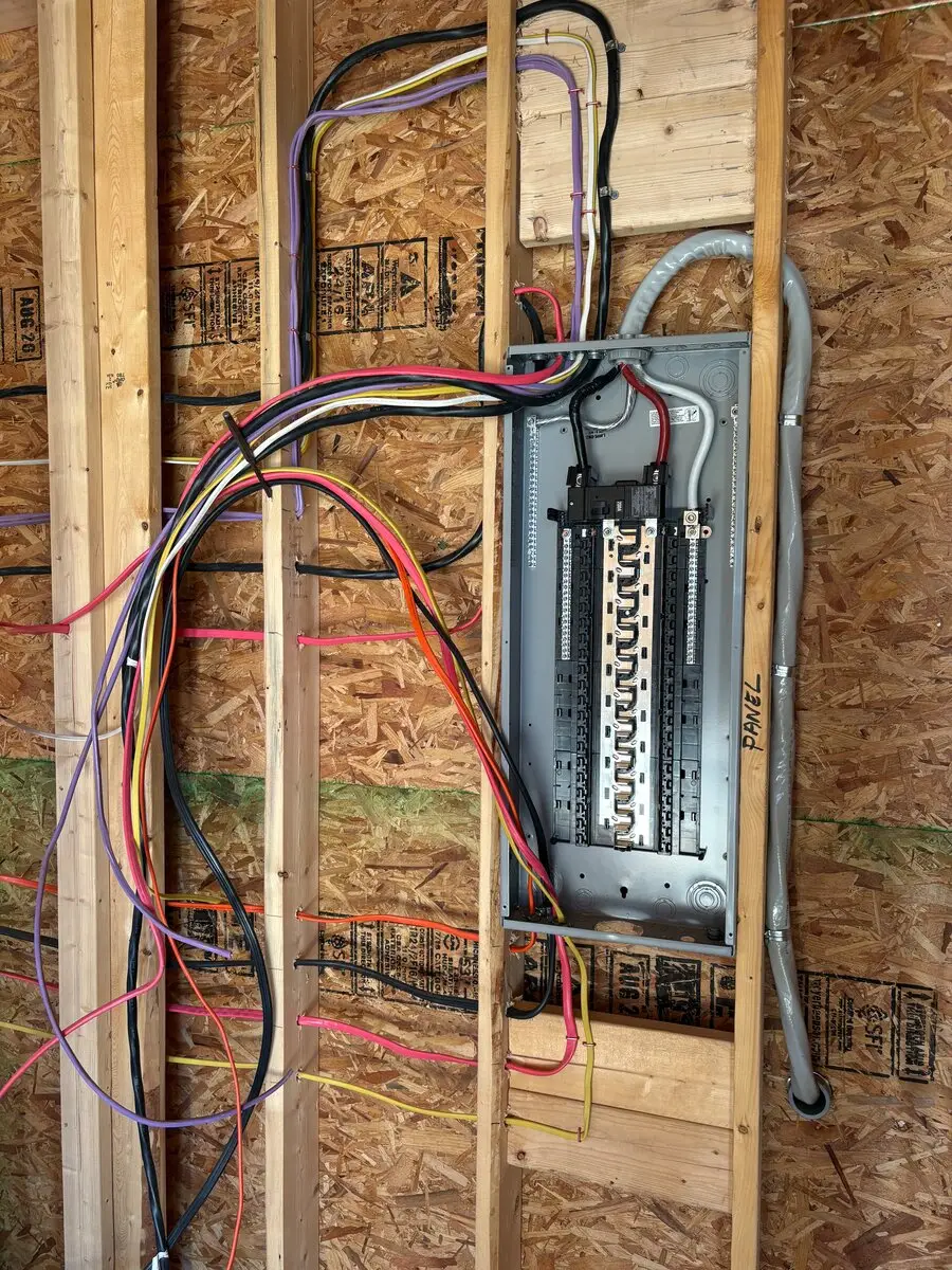 Open electrical panel between wall studs with colored wires running into it