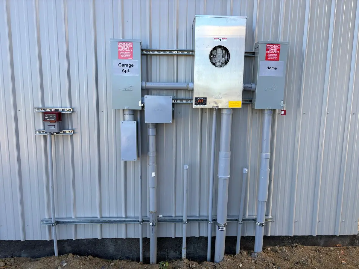 Gray electrical boxes, a meter and pipes mounted on the metal wall of a building