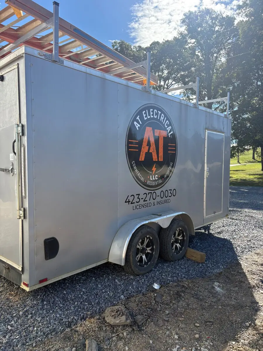 Work trailer with the AT Electrical logo and phone number on the side
